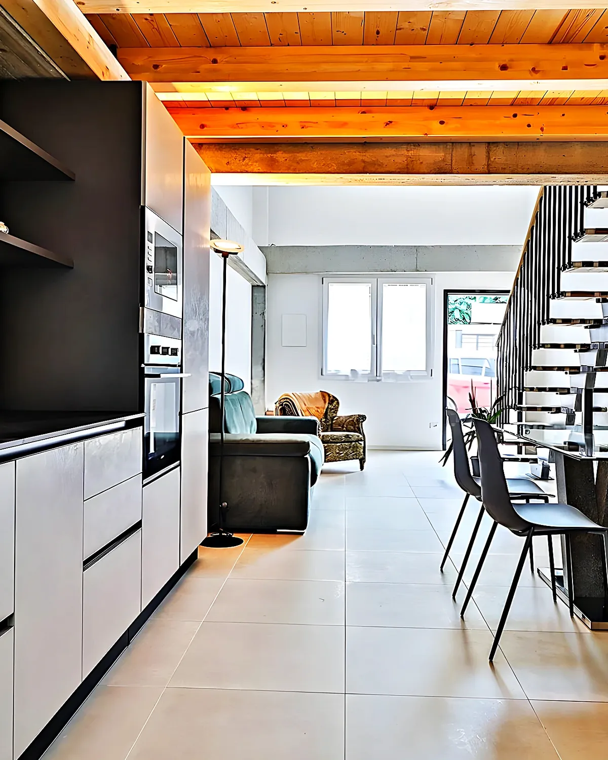Cocina blanca y negra con la escalera del dúplex al fondo, en un piso de Vilanova i la Geltrú